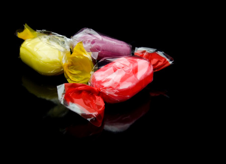 yellow, red and purple candies wrapped in cellophane foil on reflecting black surfaceの写真素材
