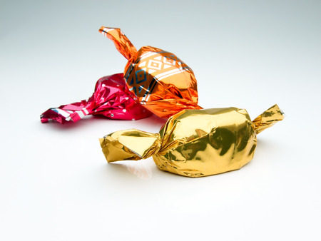 candies in red, orange and golden aluminum foil wrappers on white backgroundの写真素材