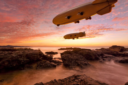Two Zeppelins gliding above a rocky coast in vibrant sunsetの写真素材