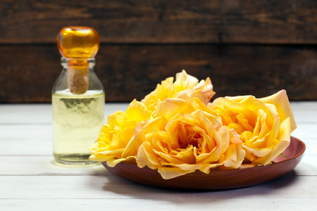 Yellow rose blossoms in wooden bowl fragrance bottle in back