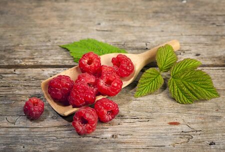heap of fresh organic raspberries on small wooden shovel arranged with leaves on rustic tableの写真素材