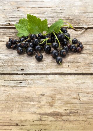 heap of organic black currant fruits and leaves on rustic wooden background with copy spaceの写真素材