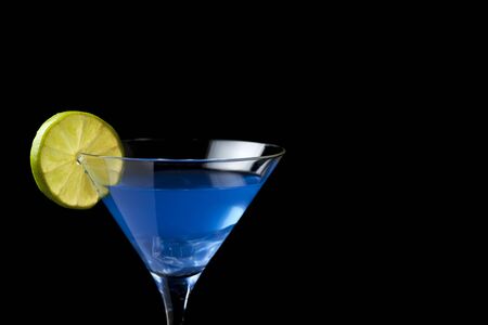 blue cocktail in martini glass with lime slice on black background with copy spaceの写真素材
