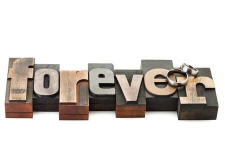 Wedding rings on the word Forever, written with vintage letterpress printing blocks isolated on white backgroundの写真素材