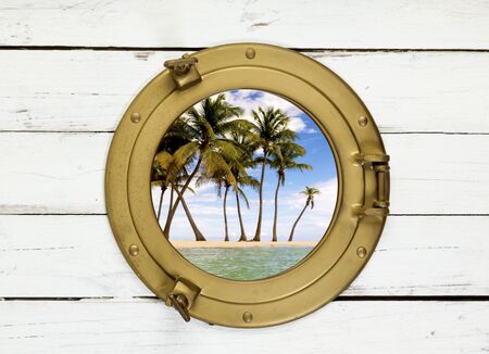 Tropical island view through brass porthole in white wallの写真素材