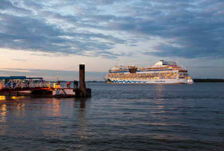 Stade, Germany - September 19, 2015: Cruise ship AIDAbella passing the pier of Stade on the Elbe river at dusk. People on the pier watching the departure.のeditorial素材
