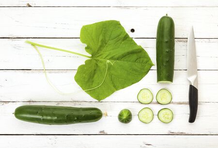 Flat lay photo of cucumbers with leaf, vine, slices, chopping knife on rustic wood backgroun, whiteの写真素材