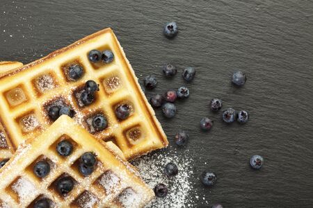 handmade belgian waffles with blueberries and icing sugar on black slate, closeupの写真素材