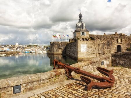 Walled Town of Concarneau with clock tower. Rusty anchor in foregrond, marina in backgroundの写真素材