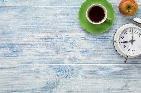 Alarm clock, coffee cup and apple on wooden background with copy space. Coffee break concept.