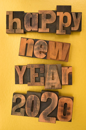 Happy new year 2020, phrase written with vintage letterpress printing blocks on gold colored...