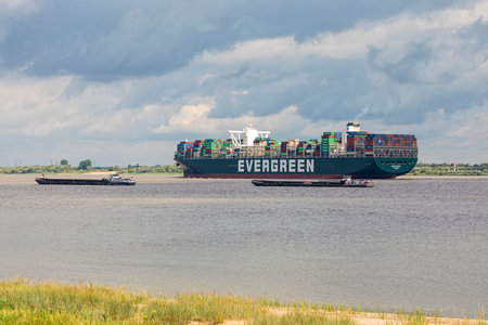 Stade, Germany - July 3, 2020: Container ship EVER GIFTED operated by EVERGREEN LINE and registered in Singapore leaving Hamburg on Elbe river passing moored riverboatsのeditorial素材
