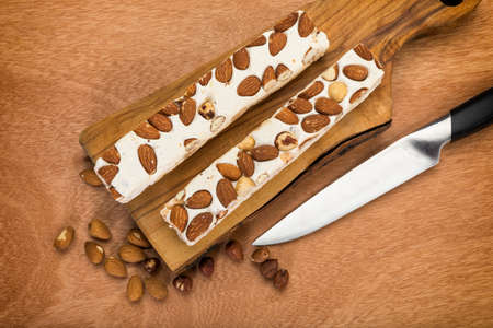Turron blocks with almonds and hazelnuts on chopping board, on wooden table, high angle viewの写真素材