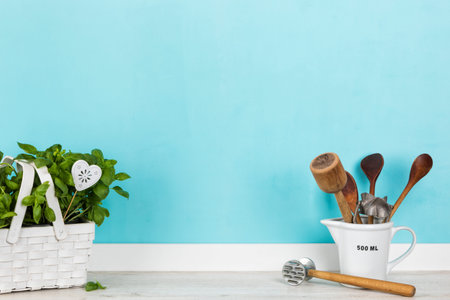 Kitchen background with a variety of vintage cooking utensils in measuring cup and basil plant in...