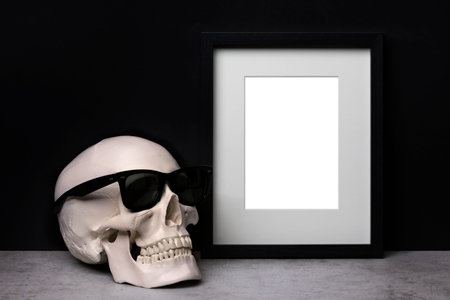 Background mockup template with black vertical picture frame with matte and human skull with...