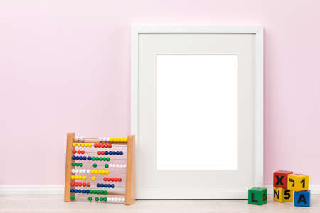 Background mockup template with white vertical picture frame with matte, aspect ratio for DIN A sizes, toy abacus and buidling blocks in foreground, all in front of pink wall. Blank area isolatedの写真素材