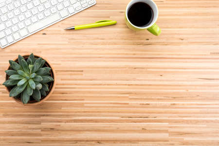 High angle view background with wooden desk, computer keyboard, coffee cup, pen and potted plant, large copy spaceの写真素材