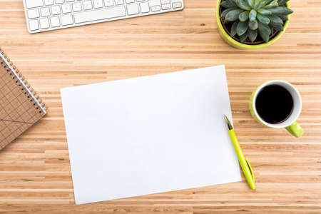 Wooden desk with computer keyboard, coffee cup, potted succulent plant, stationery and copy space on blank paper, high angle viewの写真素材