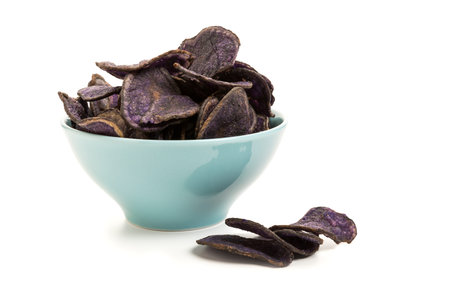 Potato chips made from purple potatoes in a turquoise bowl isolated on white backgroundの写真素材
