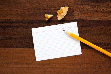blank index card with copy space, pencil and its shavings on wooden desk, flat lay