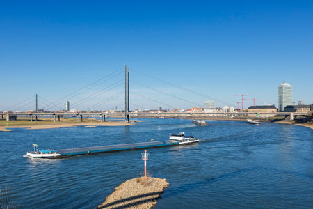 River Rhine with barges passing RheinkniebrÃ¼cke bridge at Dusseldorfの写真素材