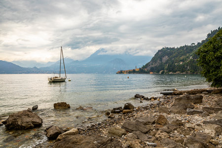 Lake Como with the town of Varenna, view from the rocky lakeside, a moored sail boat in foregroundの写真素材