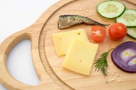 Cheese and vegetables on chopping board. Onion, cucumber, cherry tomato and sprat ingredients.の写真素材