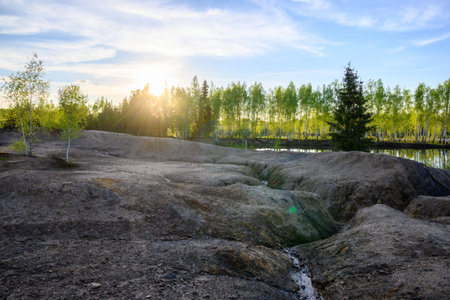 Beautiful sunset on the lake in springtime. Eroded ground in the foreground, birches and pine trees...