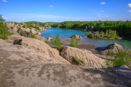 Scenic quarry lake with eroded steep slopes in the foreground and green trees in the background. Human activity result and recreation area for people.の写真素材