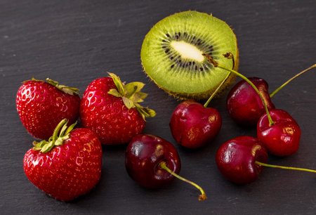 A still-life photo of fresh ripe fruits plated out on the black stone plate. Fresh strawberry,...