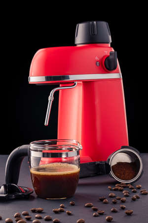 Red coffee maker with a portafilter, a glass pot and coffee beans scattered on a table against the black background. Home stuff for making espresso or cappuccino.の写真素材