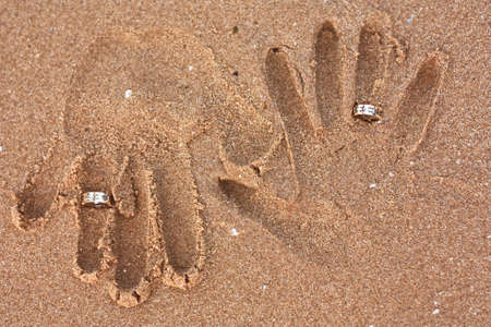honeymooners handprints in the sand with wedding ringsの写真素材