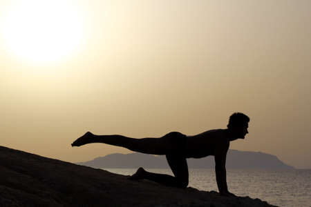 silhouette of a man doing yoga excercises on the beach at sunriseの写真素材