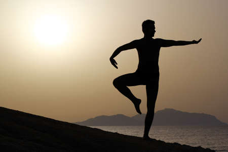 silhouette of a man doing yoga excercises on the beach at sunriseの写真素材