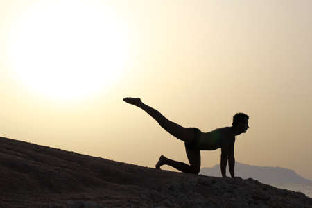 silhouette of a man doing yoga excercises on the beach at sunriseの写真素材