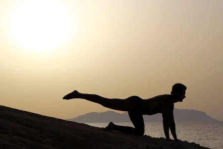 silhouette of a man doing yoga excercises on the beach at sunriseの写真素材
