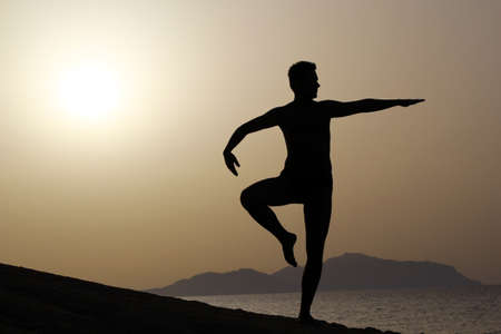 silhouette of a man doing yoga excercises on the beach at sunriseの写真素材