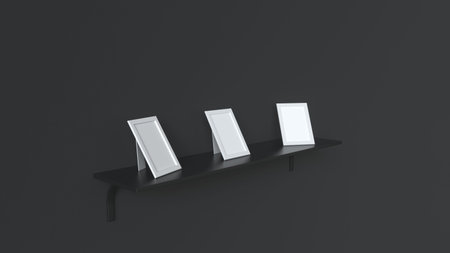 Three blank white photo frames standing on the black shelf against the black wall. Picture or photo...