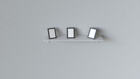 Three blank black photo frames standing on the white shelf against the white wall. Picture or photo...
