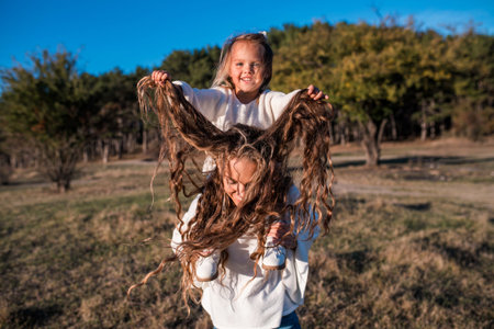 Mum and daughter having fun together outdoors. Smiling girl is playing with mothers hair. They...