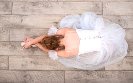 Young beautiful graceful ballerina in pointe shoes at wooden floor background. Top view, copy space. Back of ballet dancer. Ballet stretching and practice.の写真素材