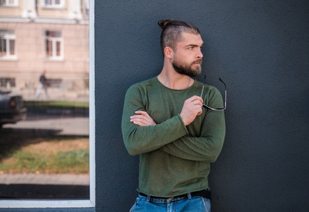 Handsome stylish man with sunglasses is standing near black wall and posing for camera. Attractive hipster full of mans charm and strength.の写真素材