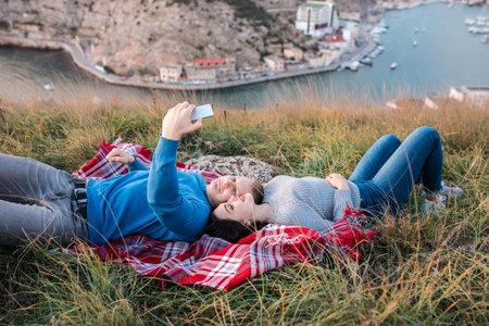 Happy young couple making selfie near coast of Black Sea. They laying on the plaid and smiling. Concept of freedom, love and travelling.の写真素材