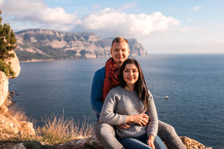 Happy couple seating on the hill near Black sea. Amazing view of the sea. Young attractive travellers smiling and hugging.の写真素材