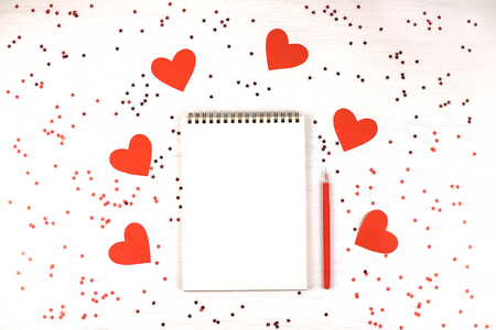 Empty note pad with festive red confetti on white wooden background. Bright and festive holiday mock up. Top view, flat lay.の写真素材