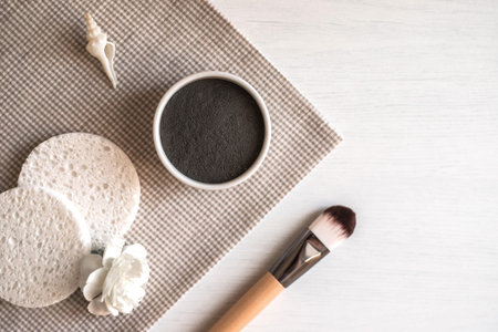 Composition with natural black cosmetic facial mask in ceramic bowl, brush, sponges, white flower...