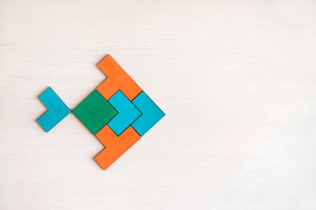 Color wooden tangram puzzle in fish shape on white wood backgroundの写真素材