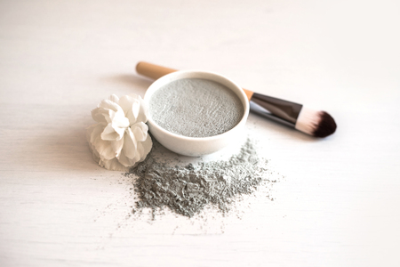Natural cosmetic facial mask in ceramic bowl on white wooden background with white flower and brush.の写真素材