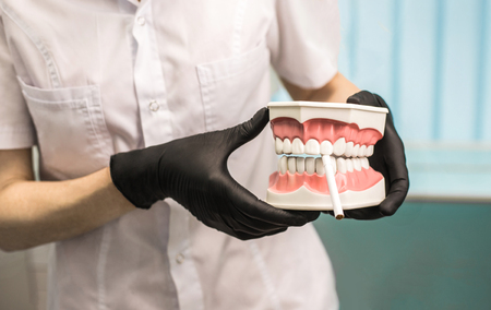 Dentists hands in black gloves hold dentures with a cigarette. Stop smoking concept.の写真素材
