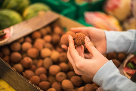 Young woman choose fresh lychee at supermarket, hand close up.の写真素材